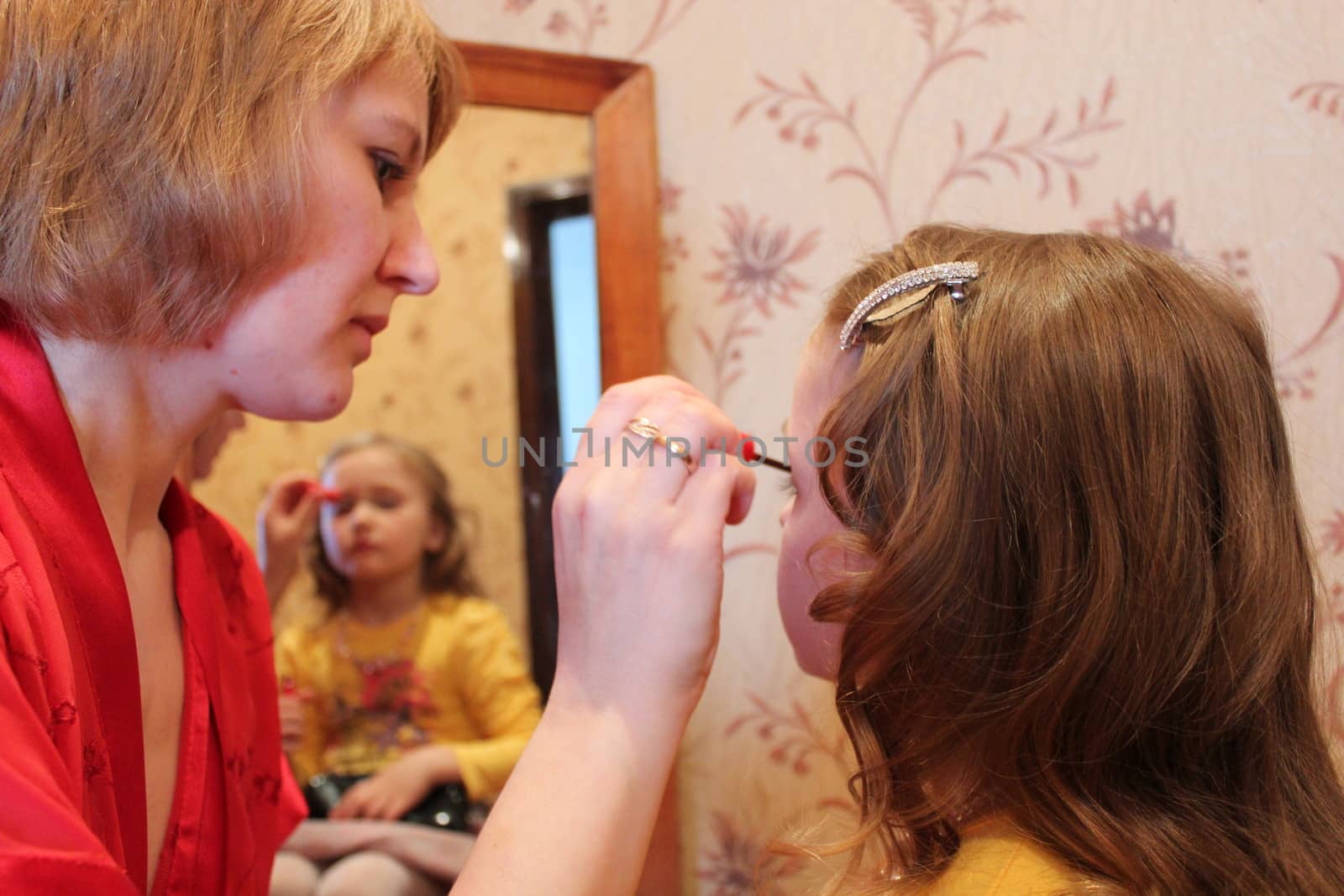 image of mother makes up daughter's face before a mirror