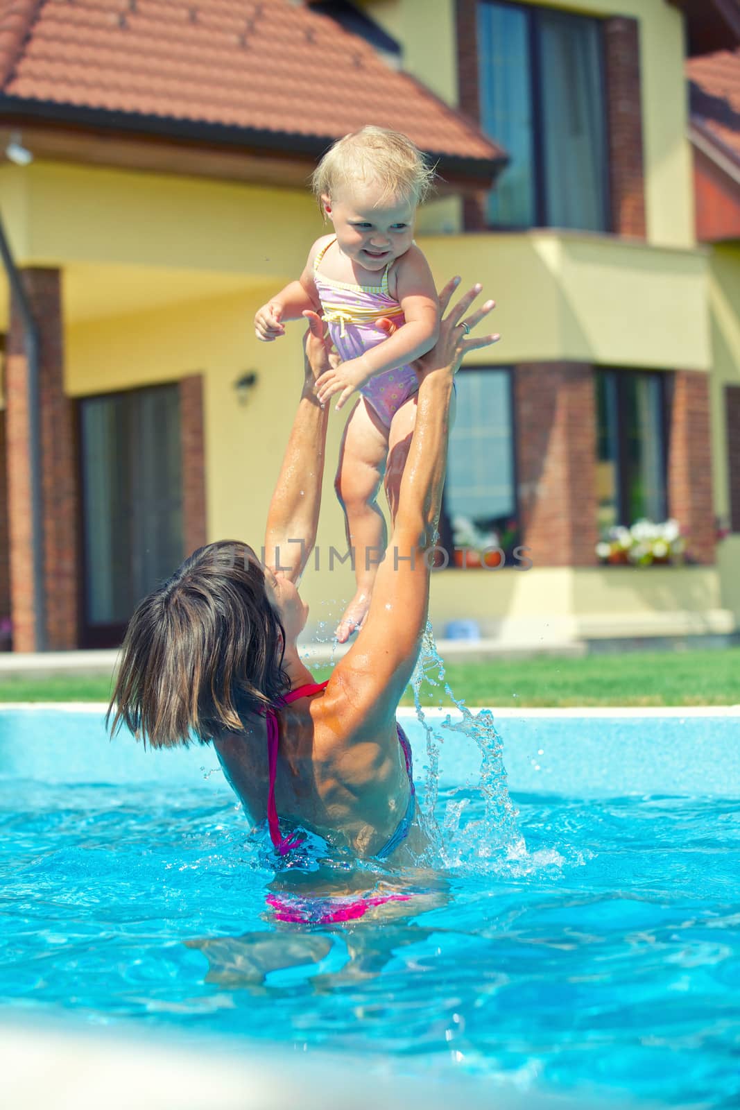 Summer vacation. Young woman plaing with her little daughter in swimming pool outdoors