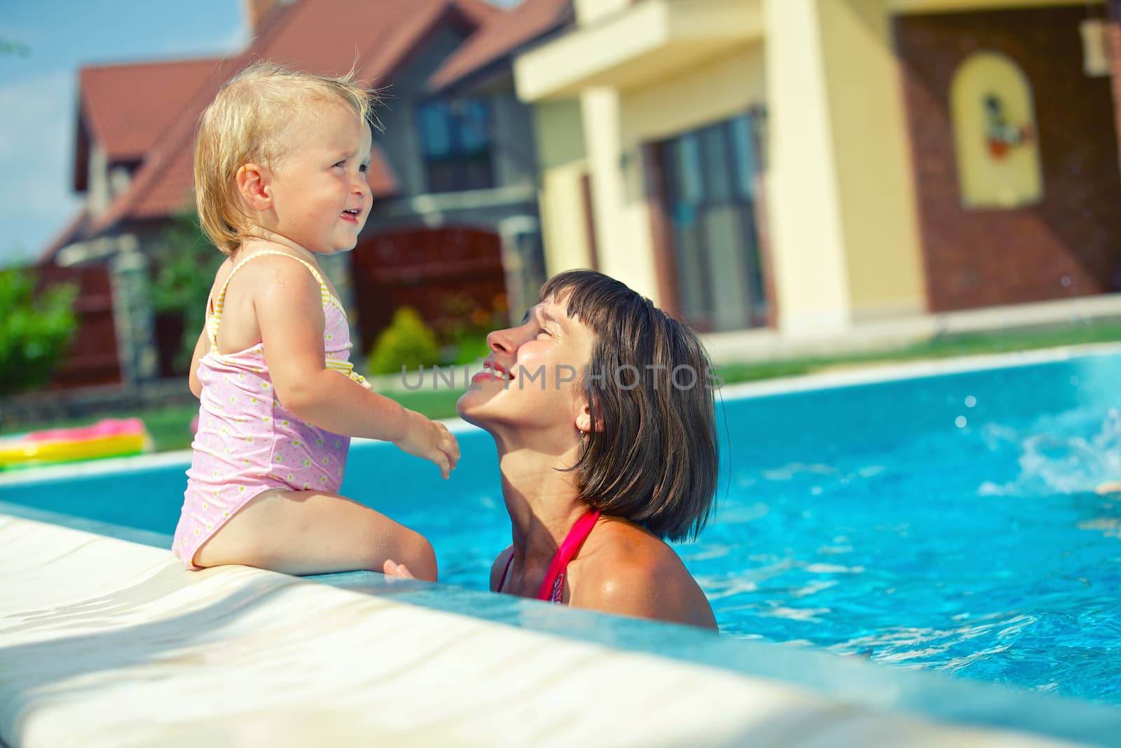 Summer vacation. Pretty little girl with her mother in swimming pool outdoors.