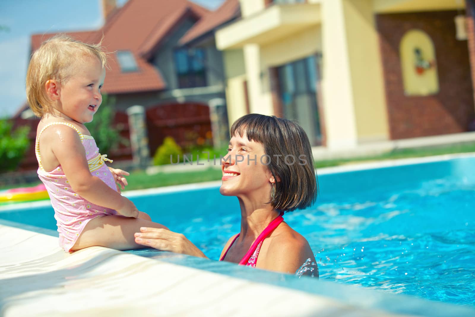 Summer vacation. Pretty little girl with her mother in swimming pool outdoors.