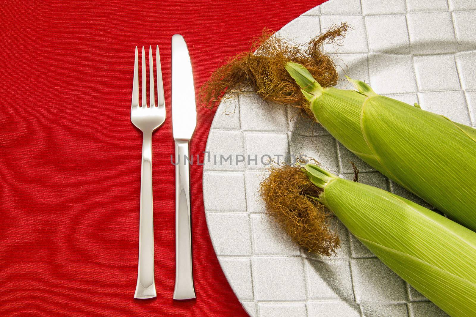 Silver Fork and knife on red table cloth and two cob on dish