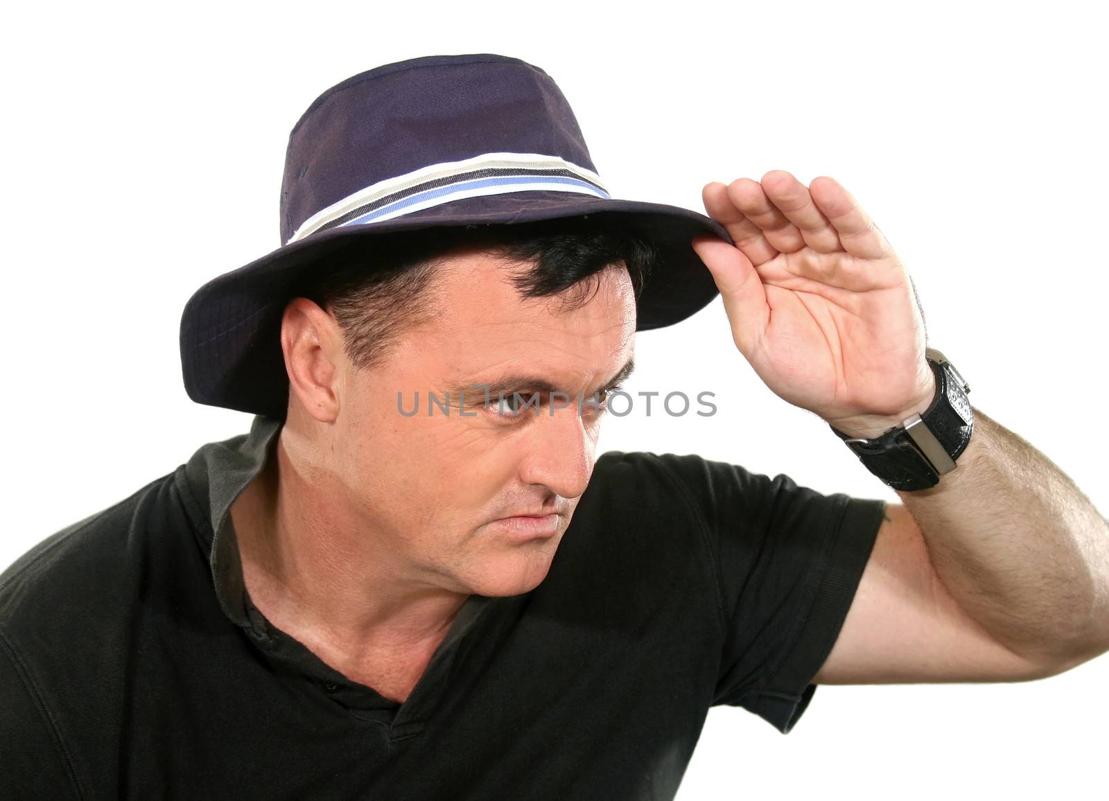 Man in hat looks away to camera right with hand on hat.