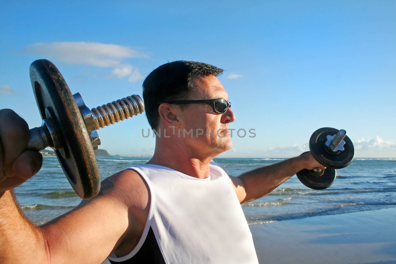 Man works out with weights on the beach just after sunrise.