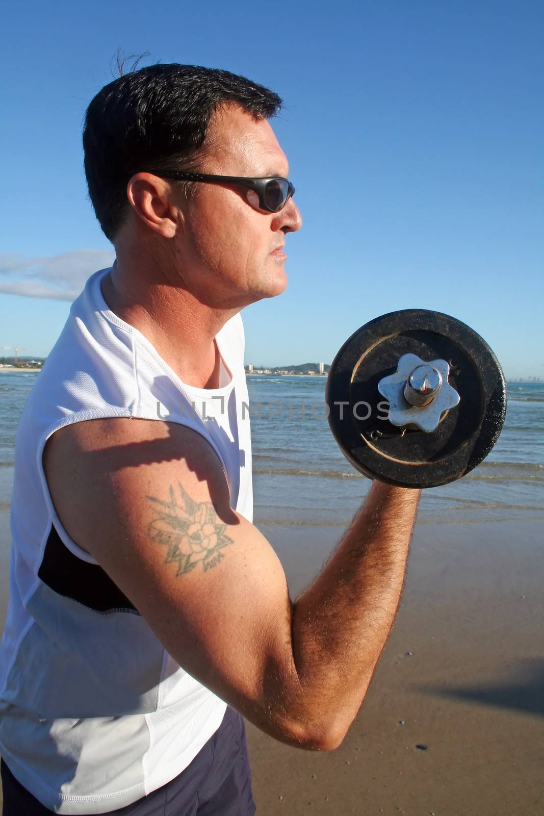 Man works out with weights on the beach just after sunrise.