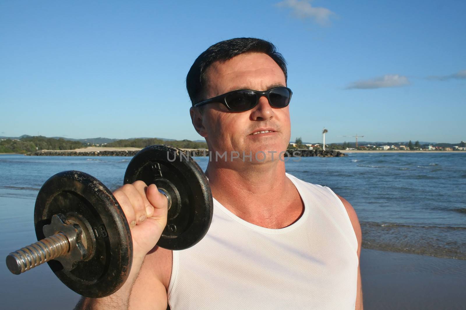 Man works out with weights on the beach just after sunrise.