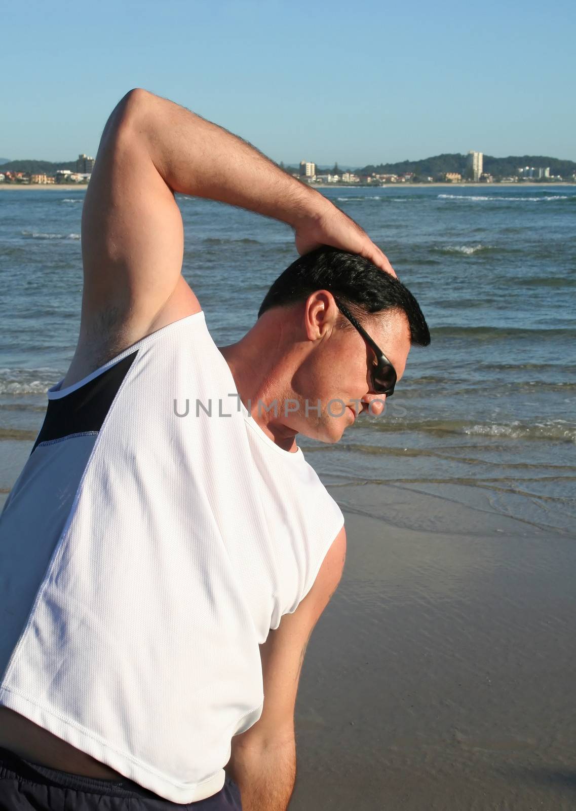 Man doing stretching exercises on the beach just after sunrise.