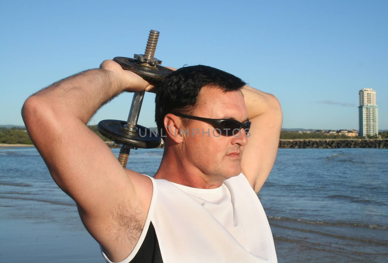 Man works out with weights on the beach just after sunrise.