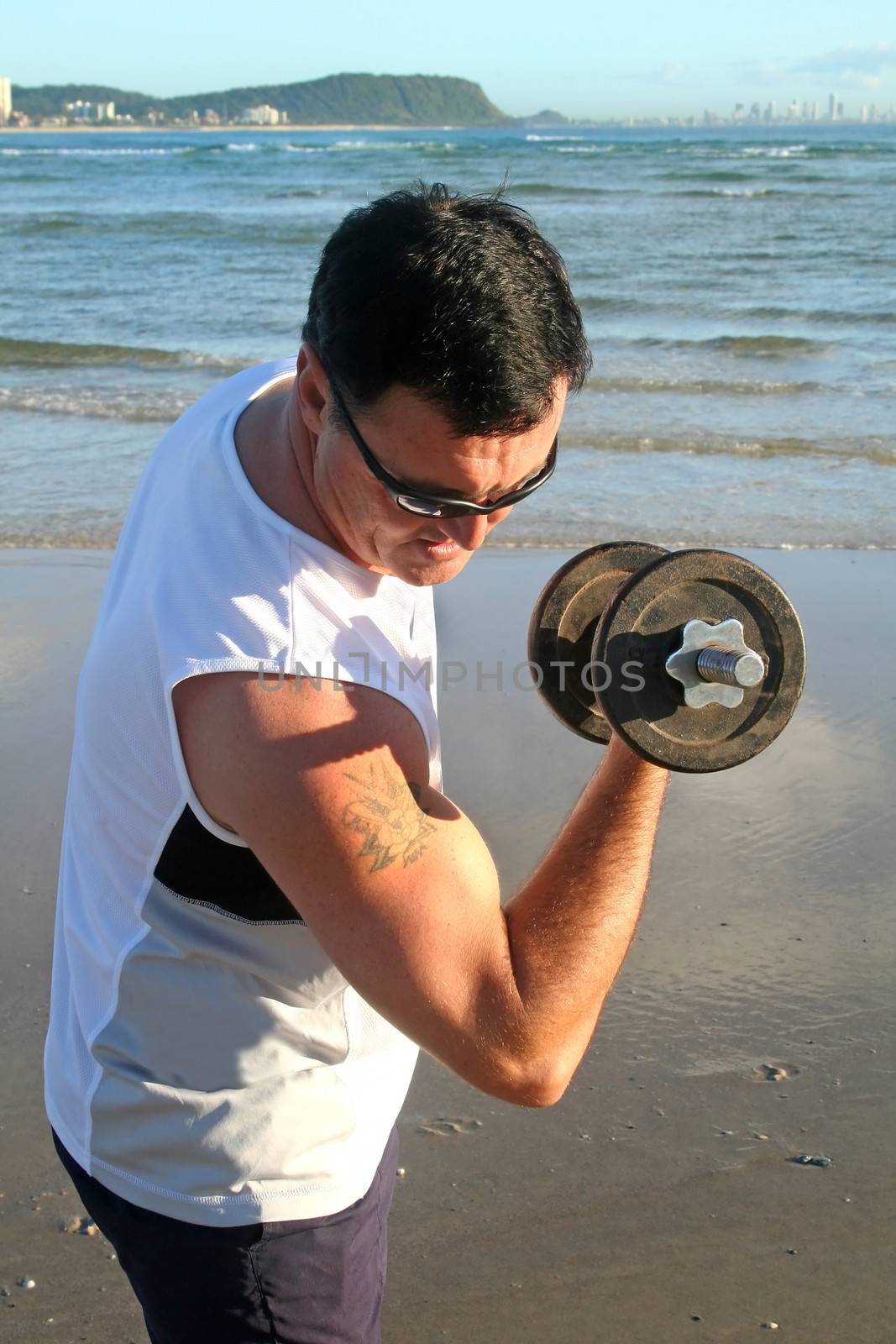 Man works out with weights on the beach just after sunrise.