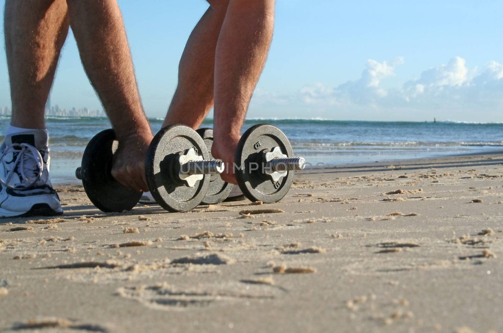 Man picks up work out weights on the beach at sunrise.