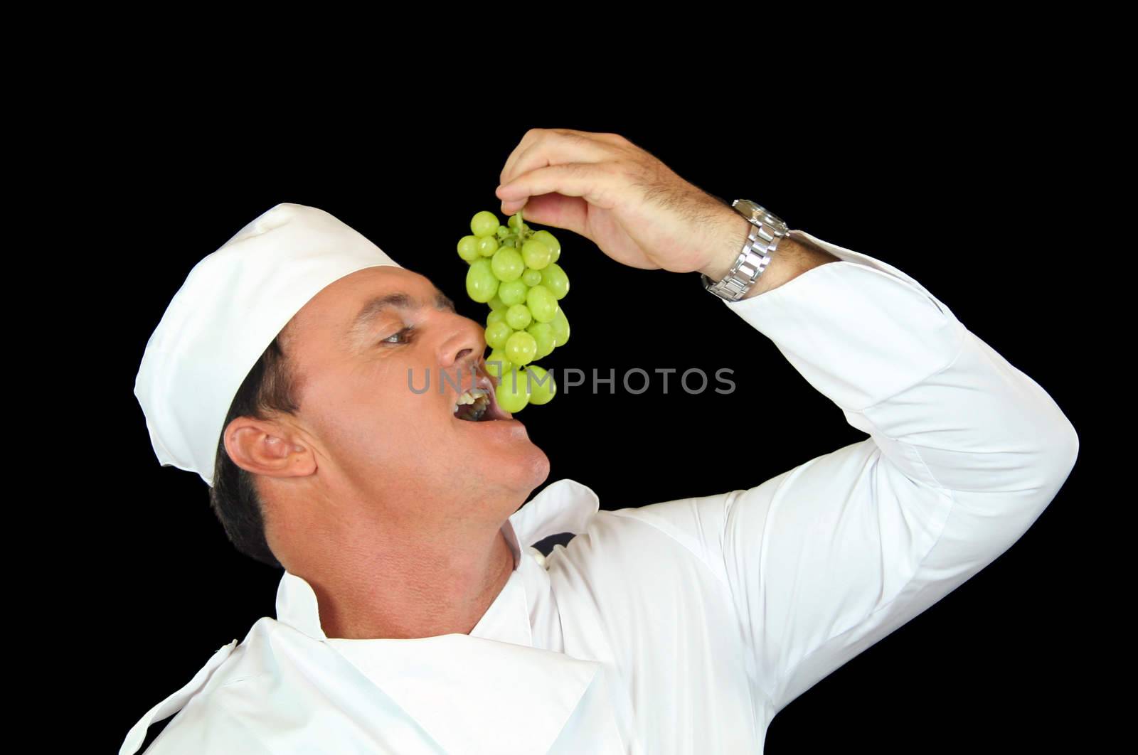 Chef lifting a bunch of grapes to his mouth to eat.