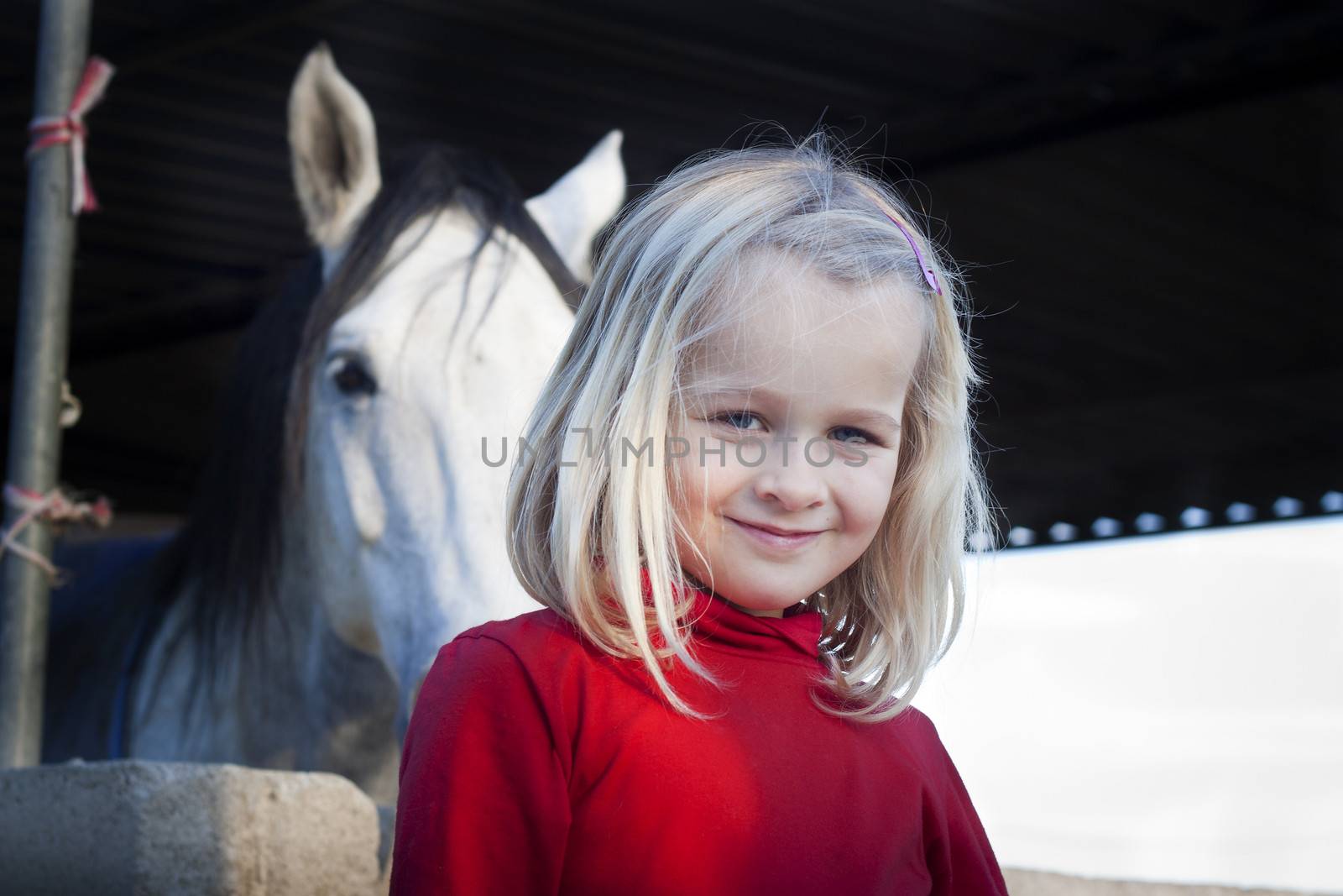 A young child standing in front of her horse, looking at the camera, positive feeling