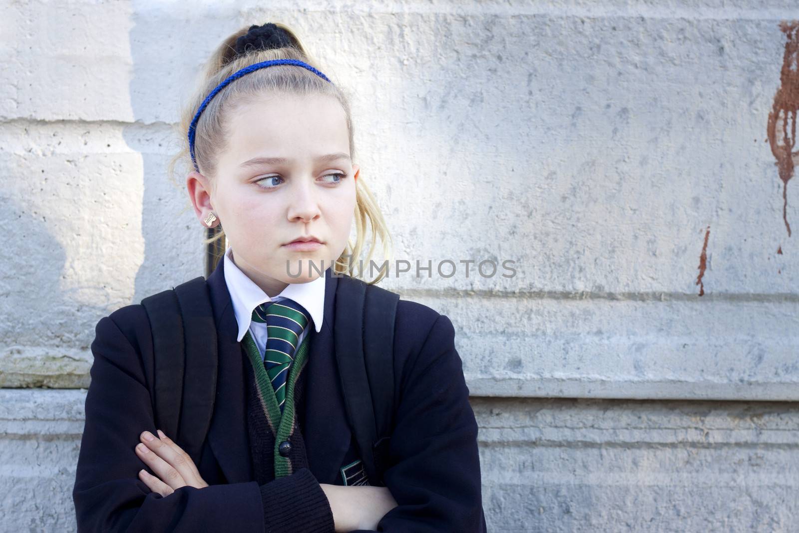 Teenage kid in school uniform looking angry, standing against a concrete wall with graffiti. Real people, candid shot