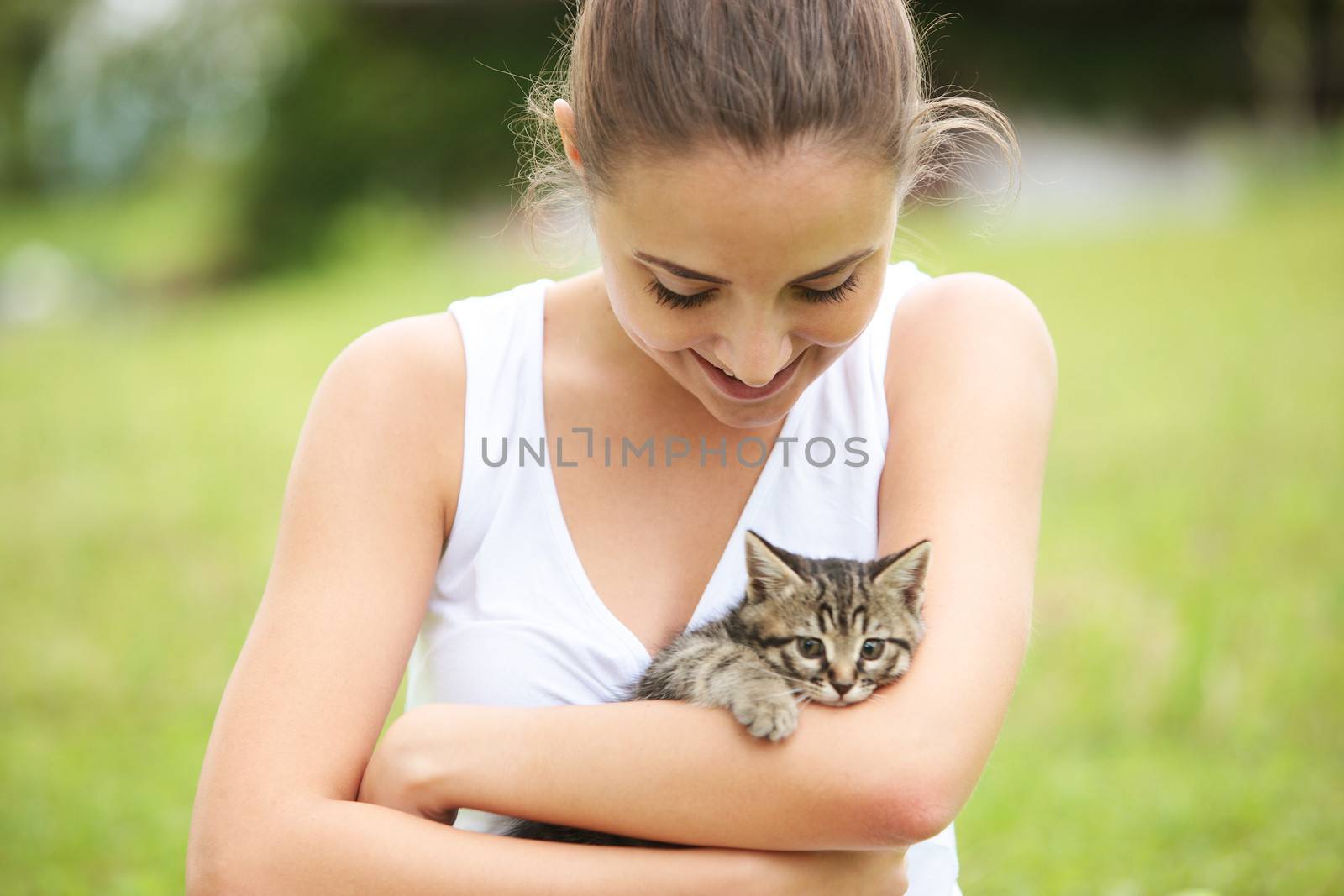 Beautiful young woman embracing a cute kitten outdoors