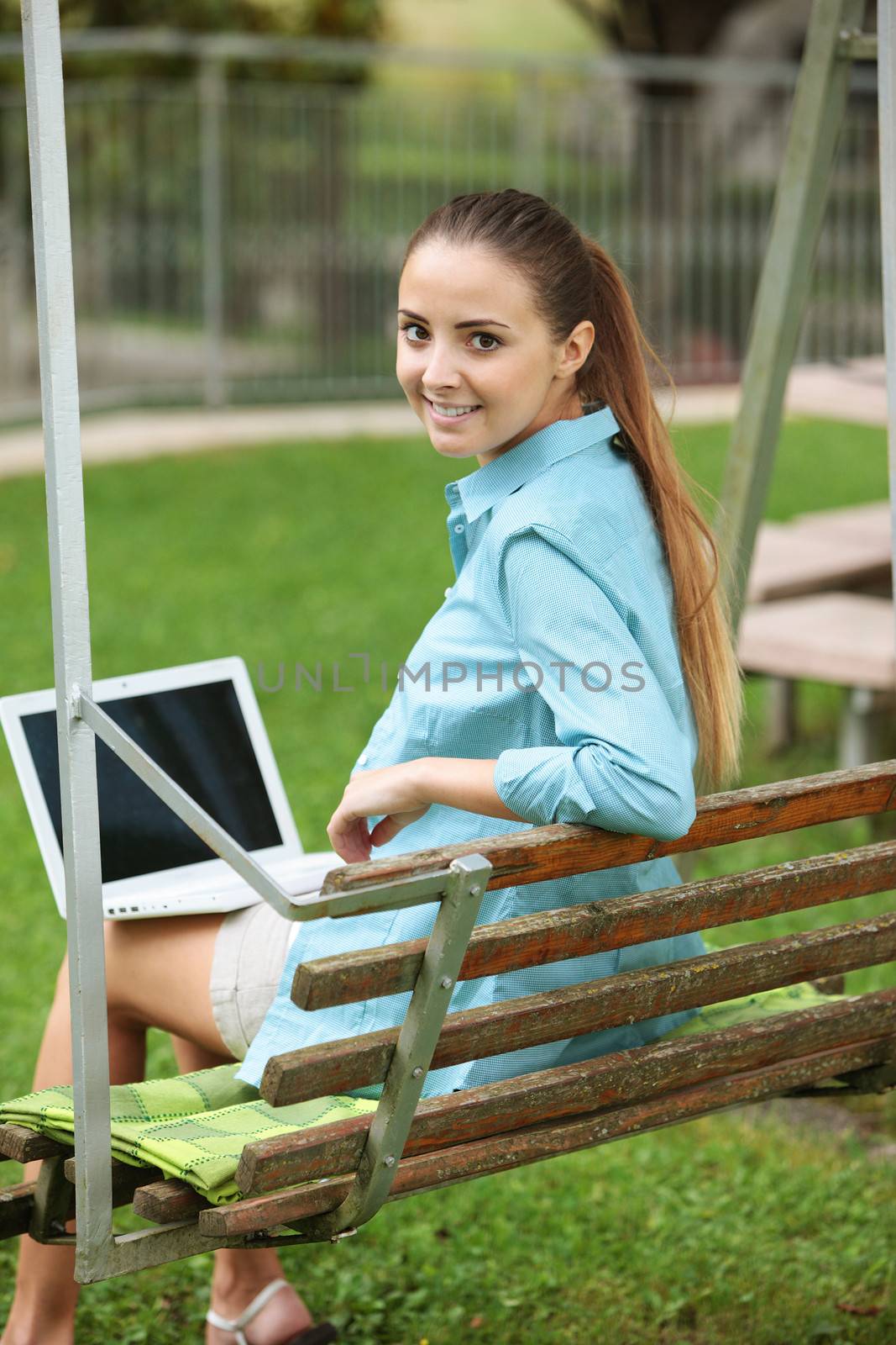 Cheerful girl working in laptop outdoors sitting on seesaw