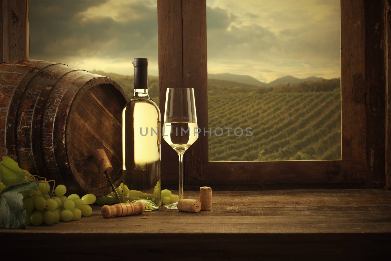 Wine bottle and wineglass on wooden table, vineyard on background