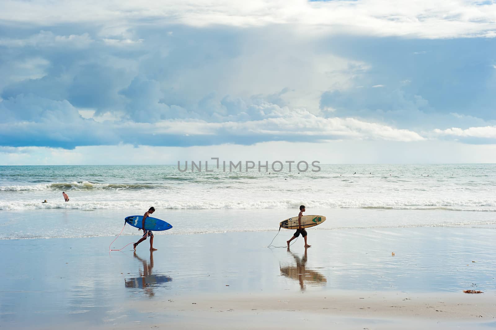 Bali island; Indonesia - March 16, 2013: Local boys walking with a surfboards on the beach. Bali is one of the top of world surfing destinations.