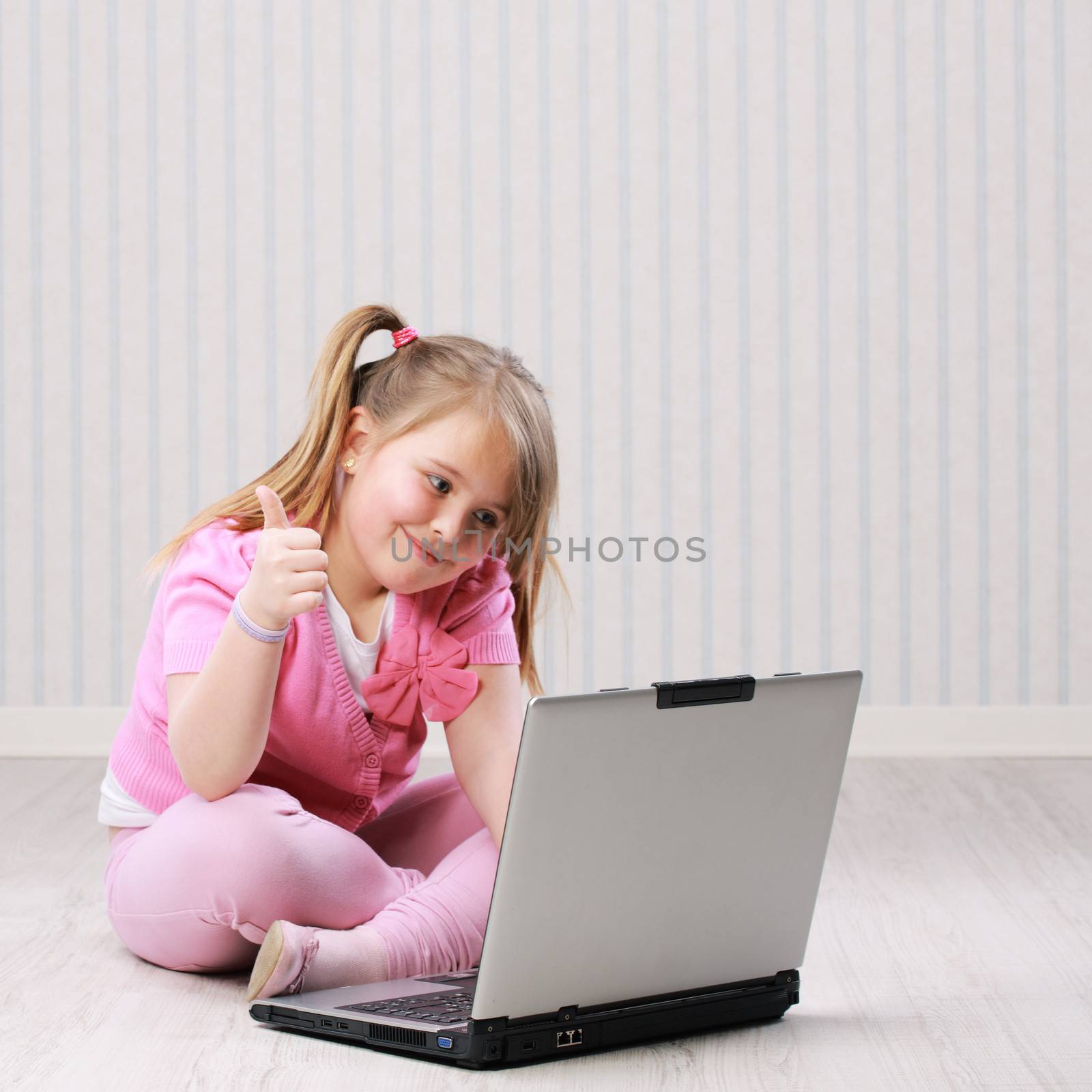 Cute little girl working on a notebook computer showing thumbs up