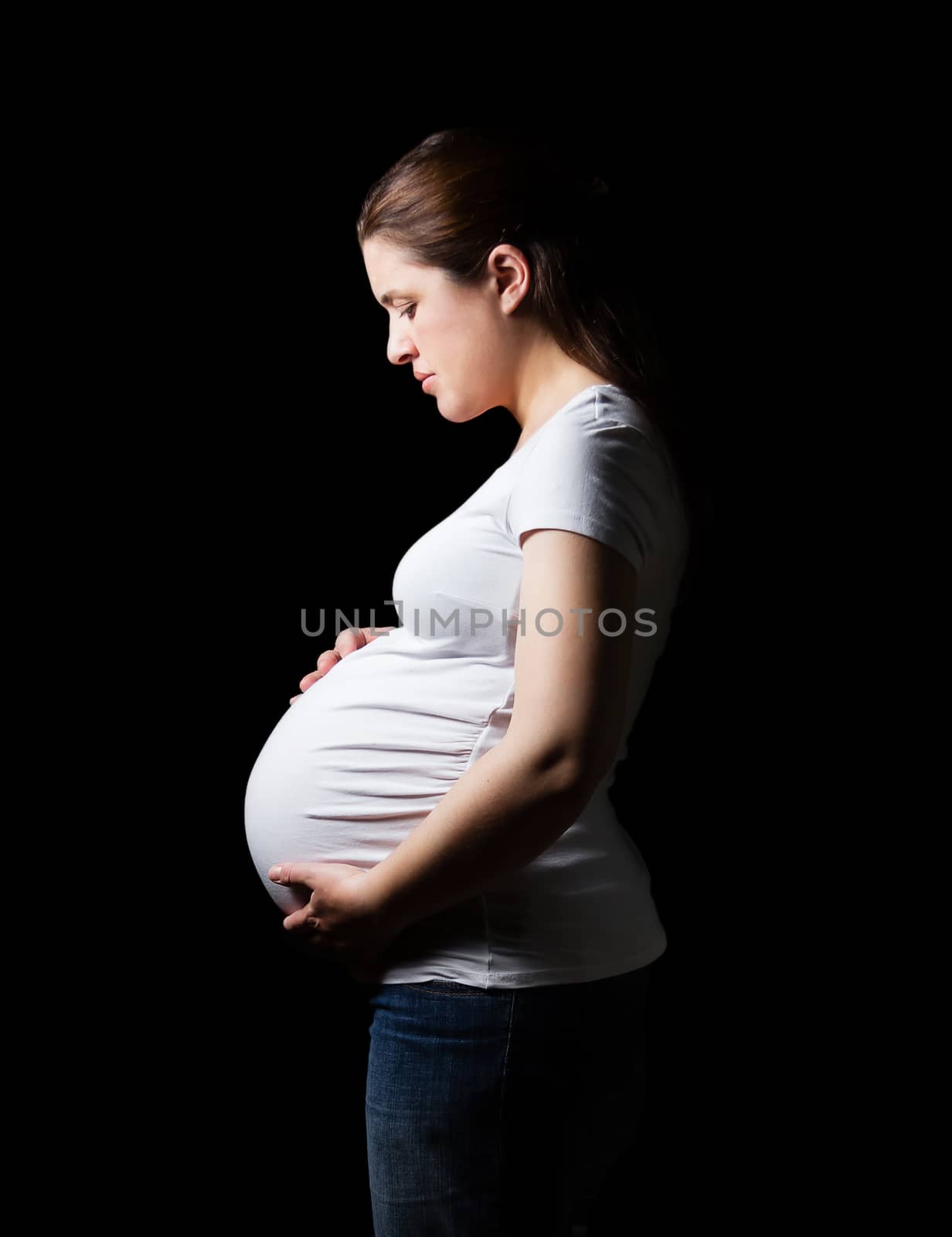 Beautiful expectant pregnant woman looking her belly isolated over a black background