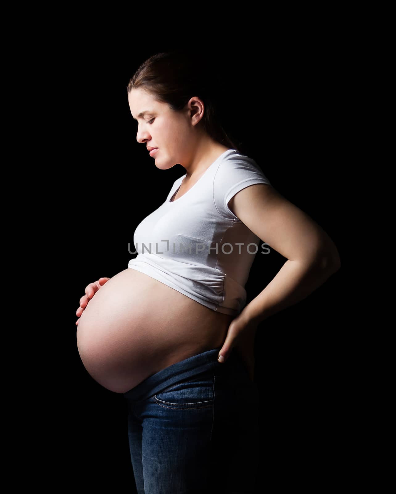 Beautiful expectant pregnant woman looking her belly isolated over a black background