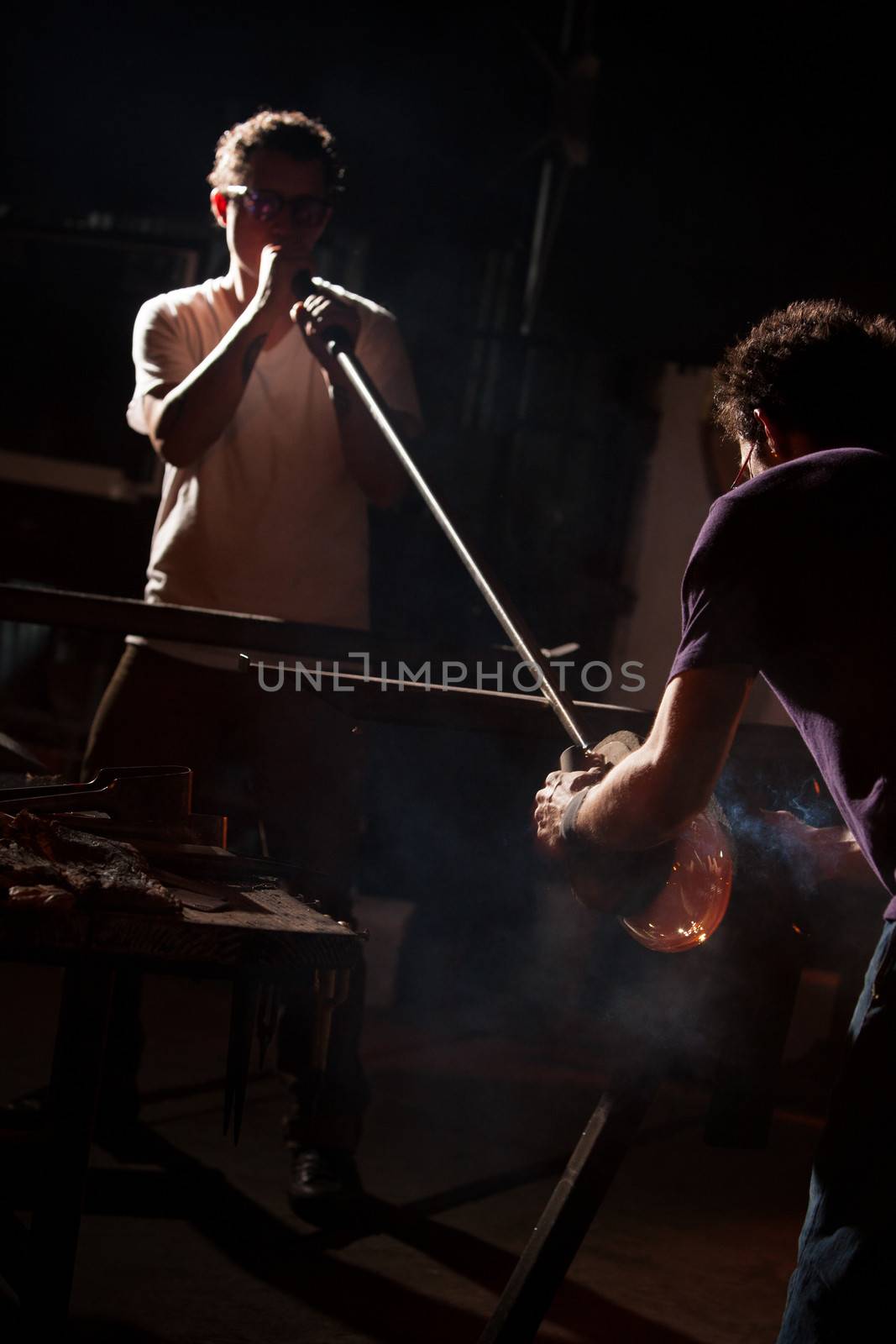Two glass artists using blowpipe to create glass object
