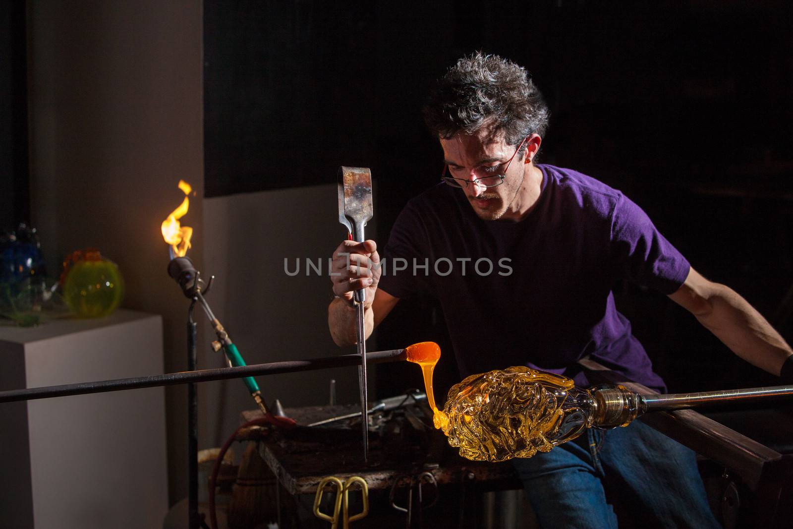 Worker using pliers and rod to decorate glass object