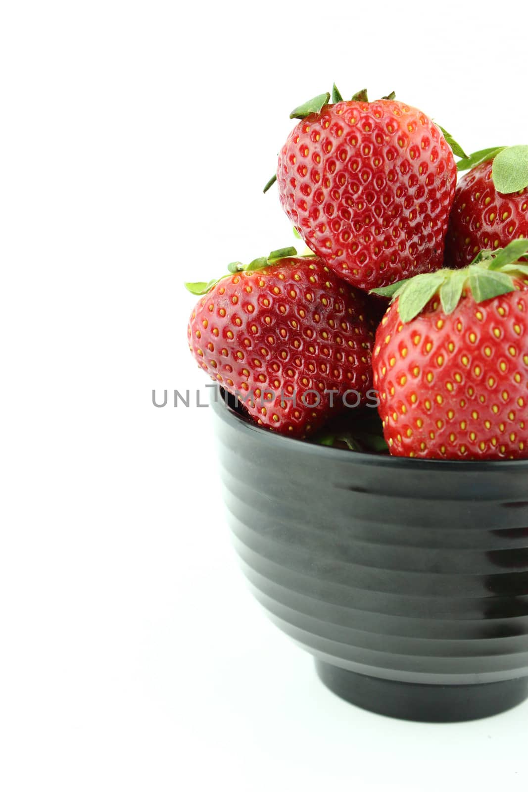 Strawberries into black bowl isolated over white background