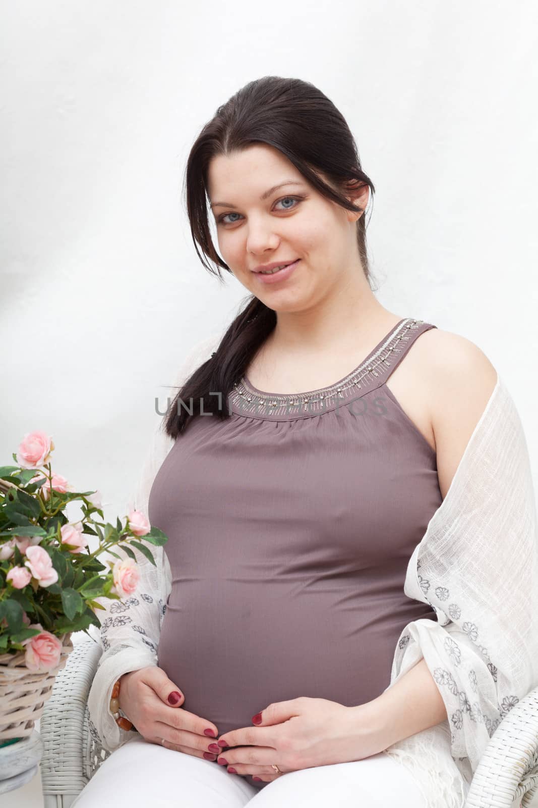 Happy pregnant woman sits in the room with flowers