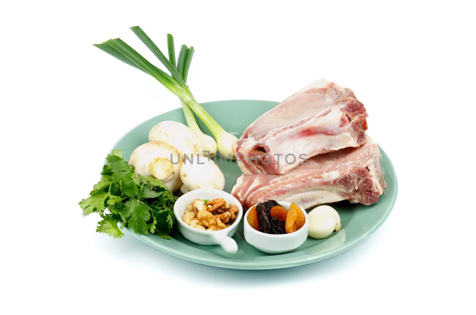 Raw Pork Chops and Ingredients with Edible Mushrooms, Greens, Nuts, Garlic and Dried Fruits on Green Plate isolated on white background