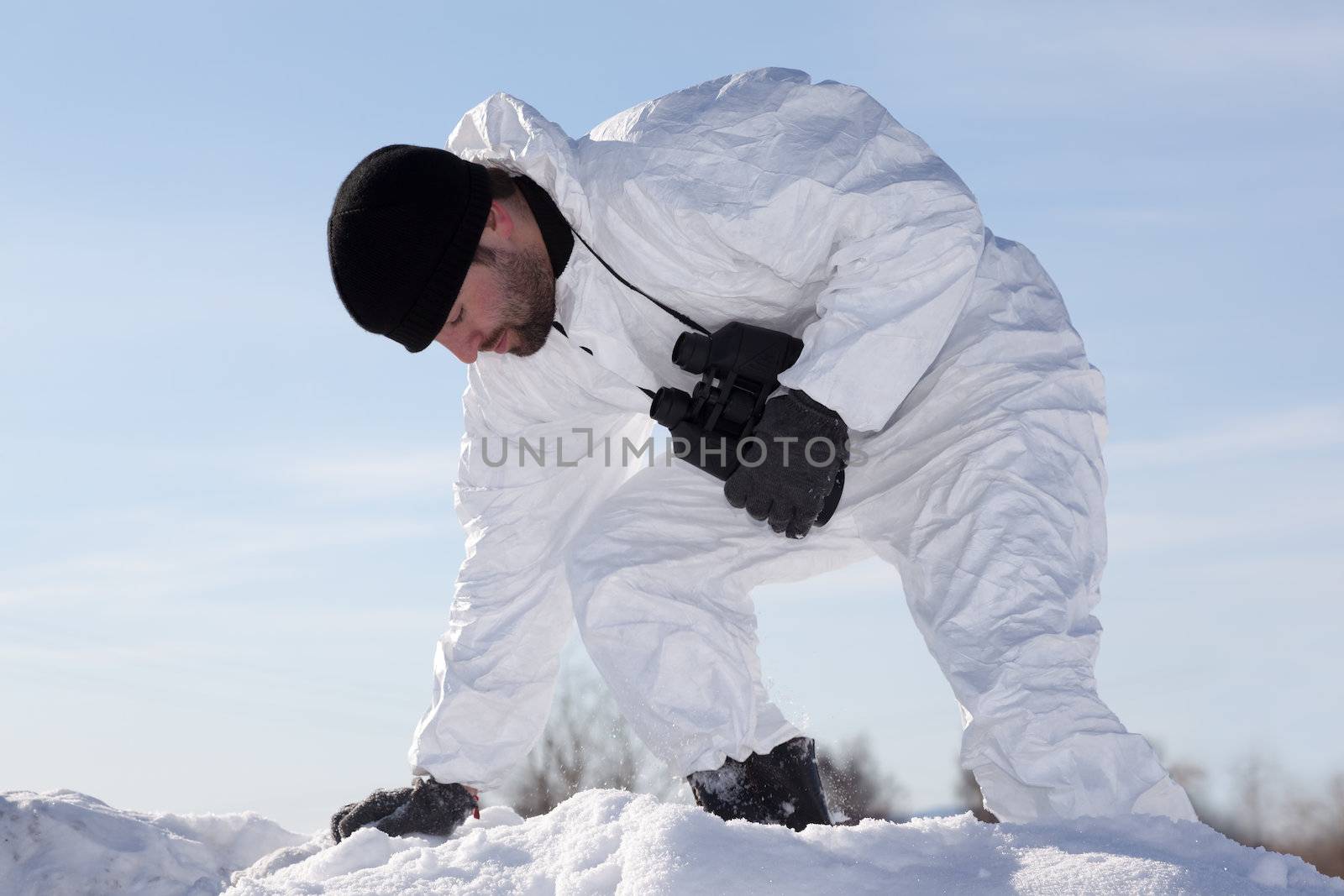 
Wounded soldier in white camouflage sneaking through the mountains. Against the background of blue sky in winter sunny day
