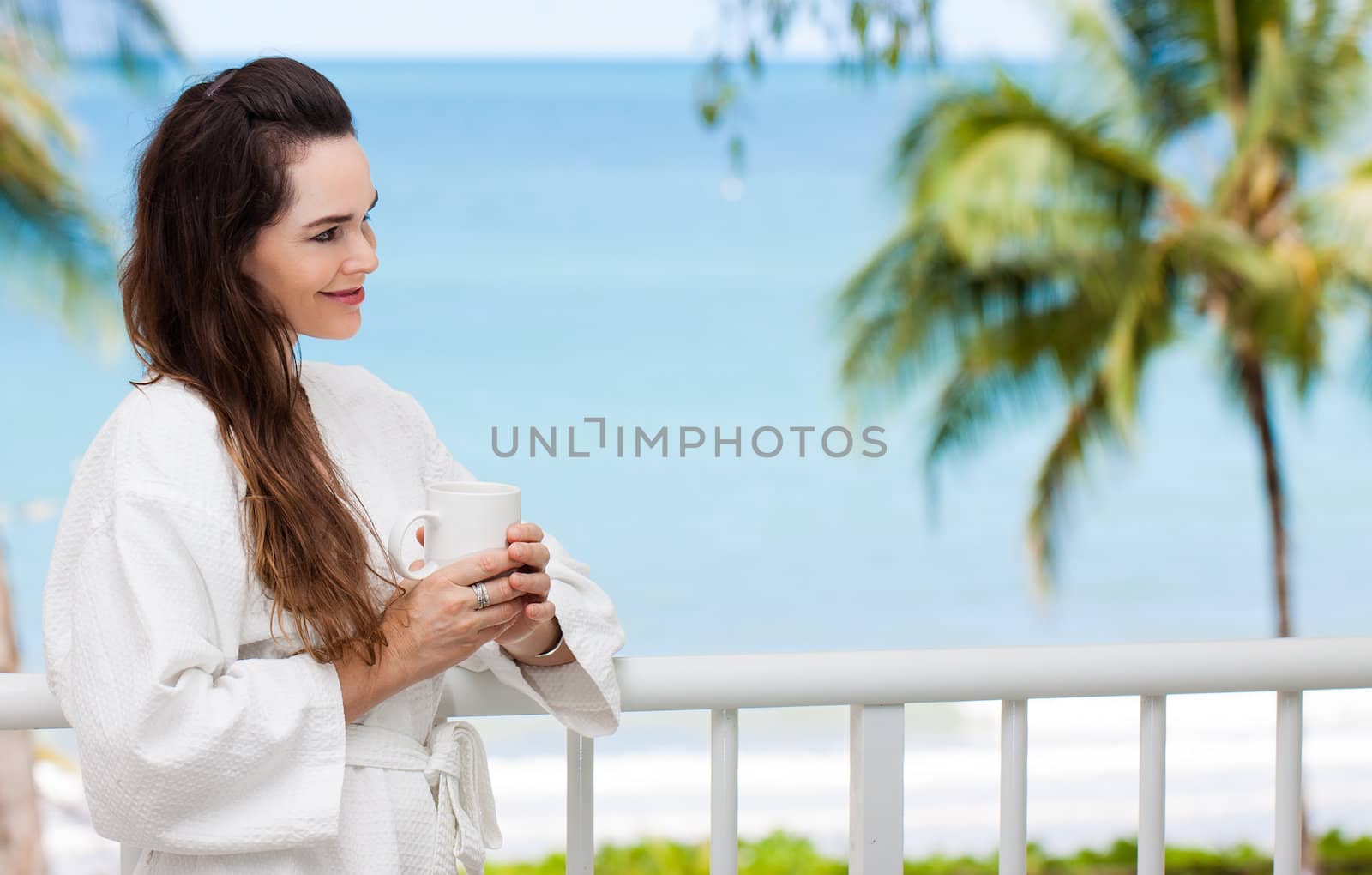 Portrait of a beautiful woman relaxing wit her breakfast coffee or tea on a tropical balcony.