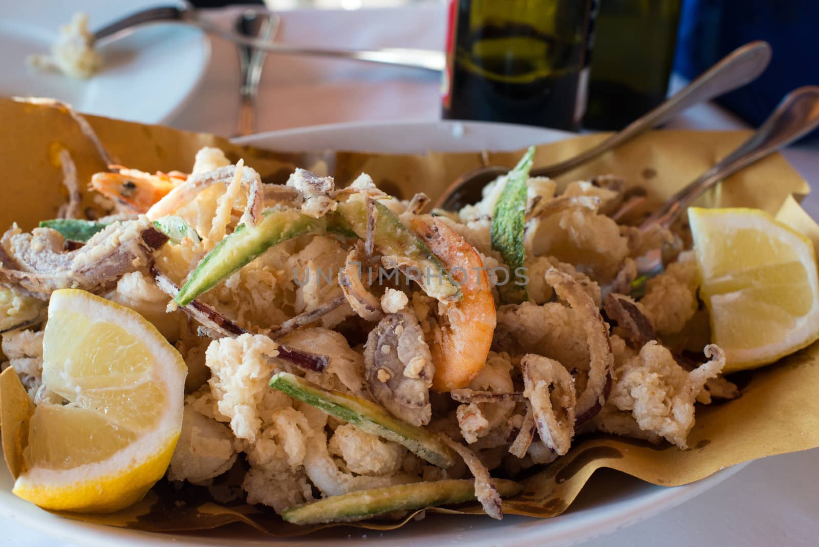 Deep batter fried seafood, squid rings , calamari and scampi with vegetables and lemons on white plate in a restaurant