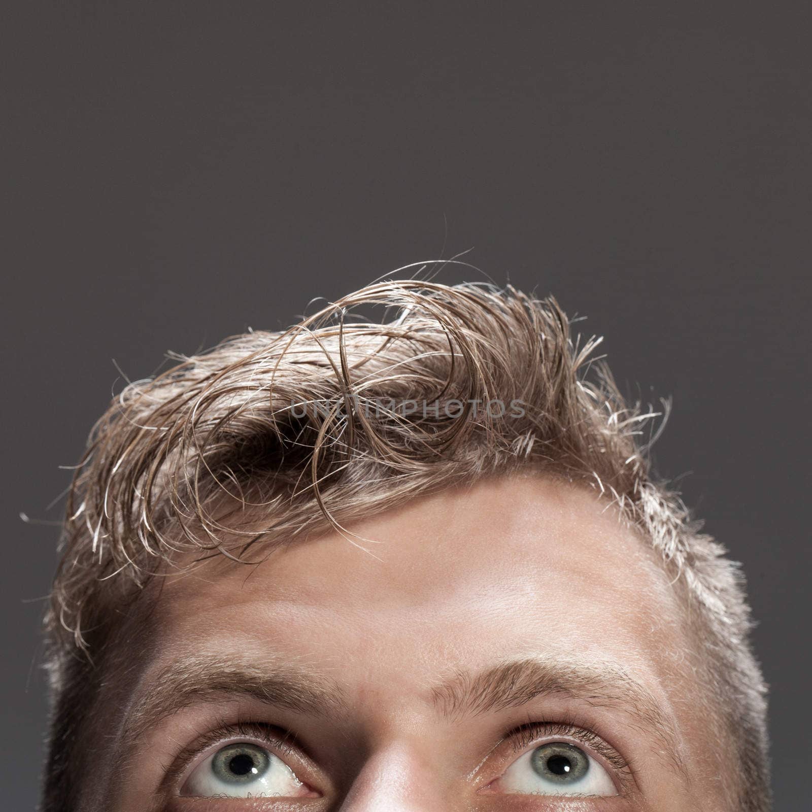 Young caucasian man looking up over grey background