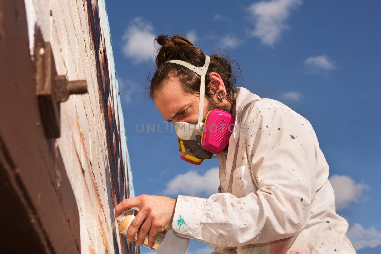 Graffiti artist with respirator spray painting a wall