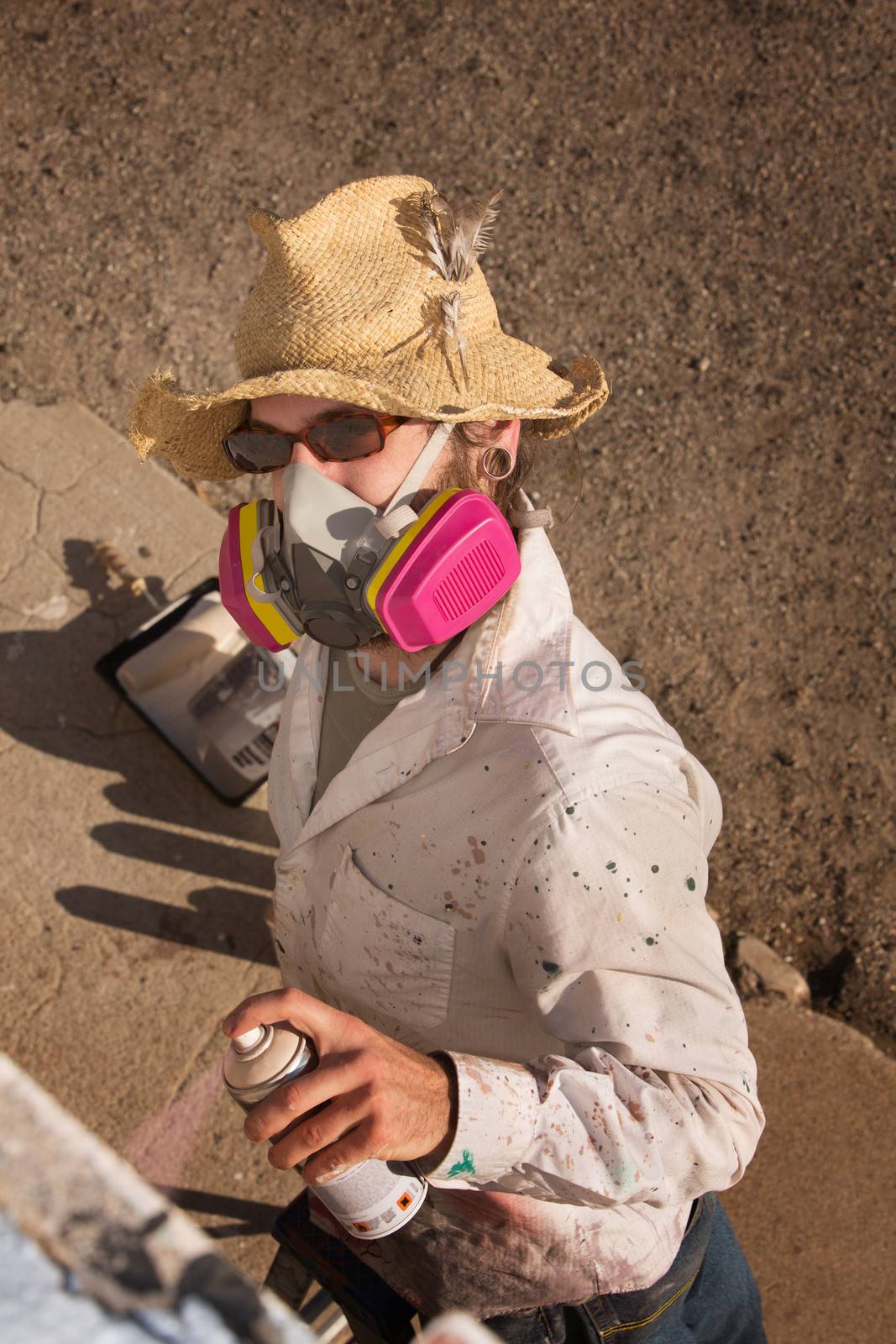 Person with hat and sunglasses spray painting a wall