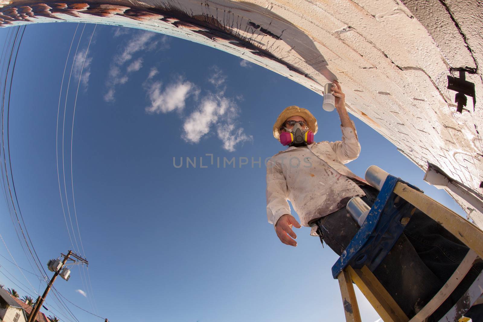 Wide angle view of disguised graffiti artist working on mural