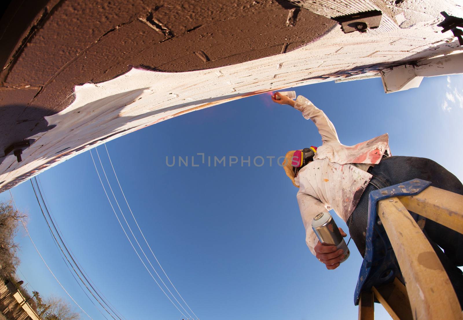 Graffiti artist standing on ladder and painting mural