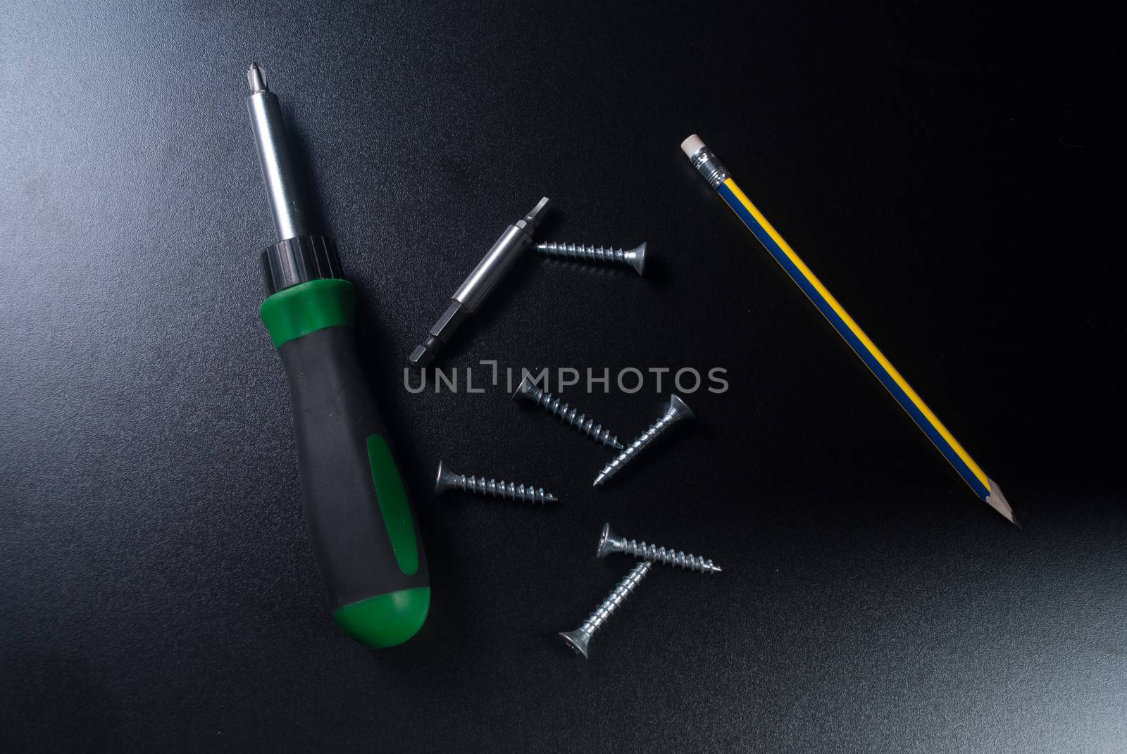 Screws, screwdriver and pencil on black background.