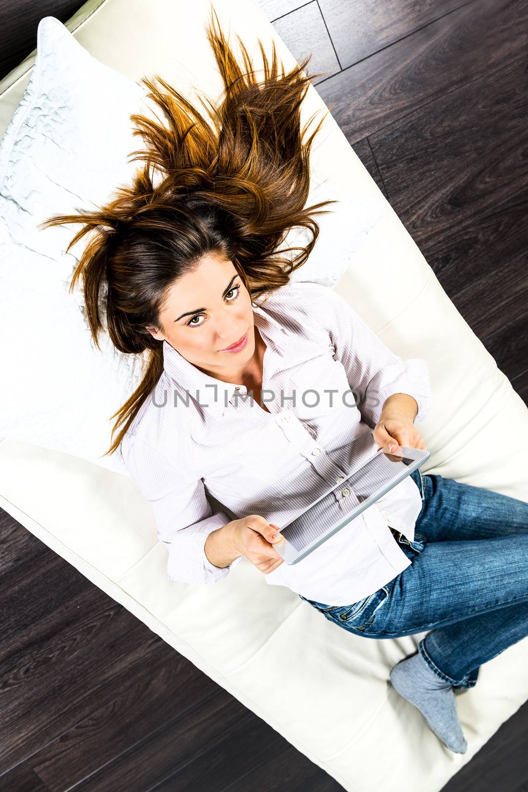 Young woman lying on sofa with electronic pad