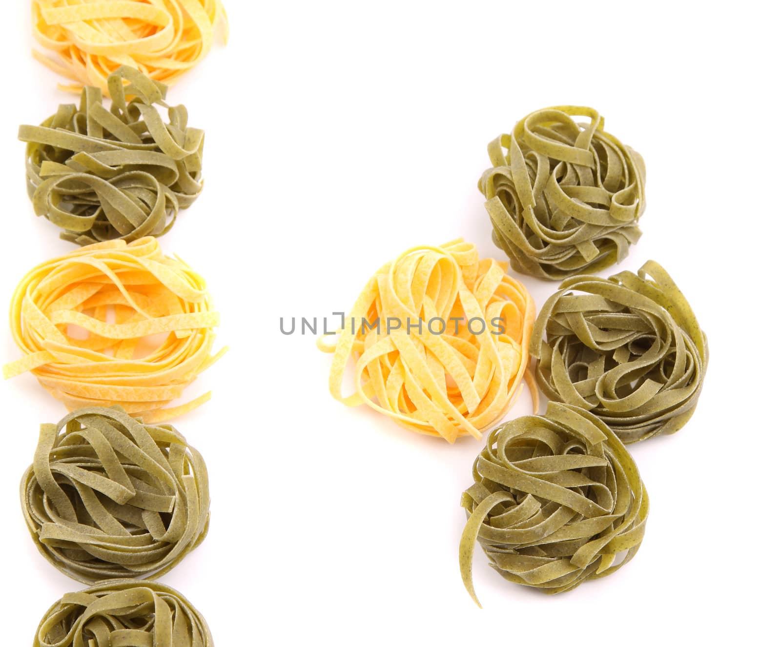 Yellow and green uncooked tagliatelle on white background