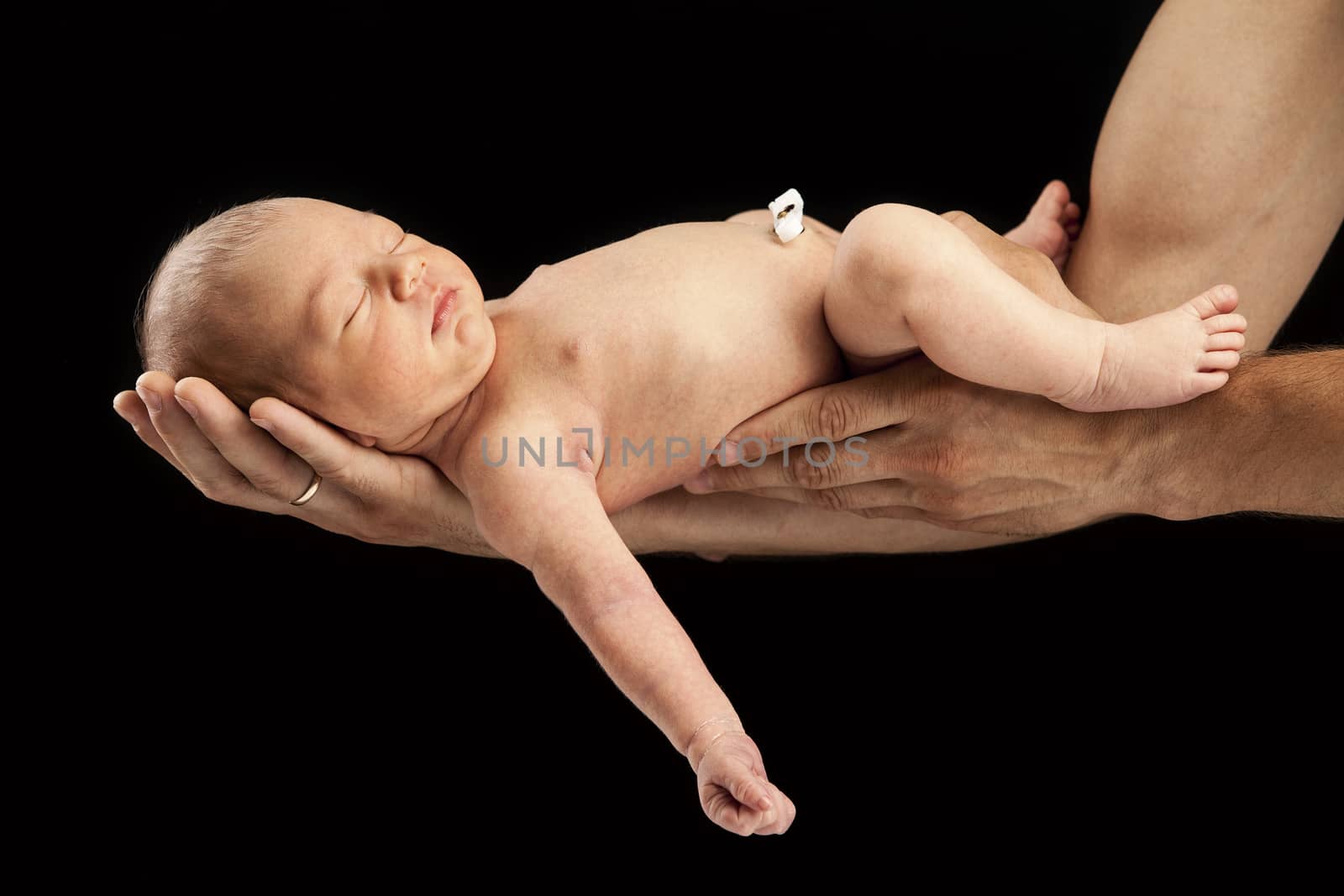 Newborn boy lying on his dad's arms over black