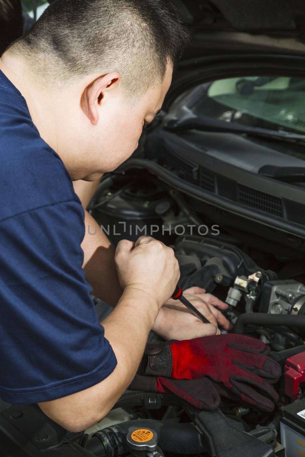 An Asian car mechanic fixing a car. 