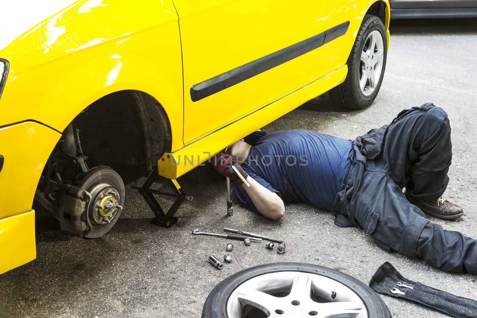 A mechanic underneath a yellow car doing maintain job.