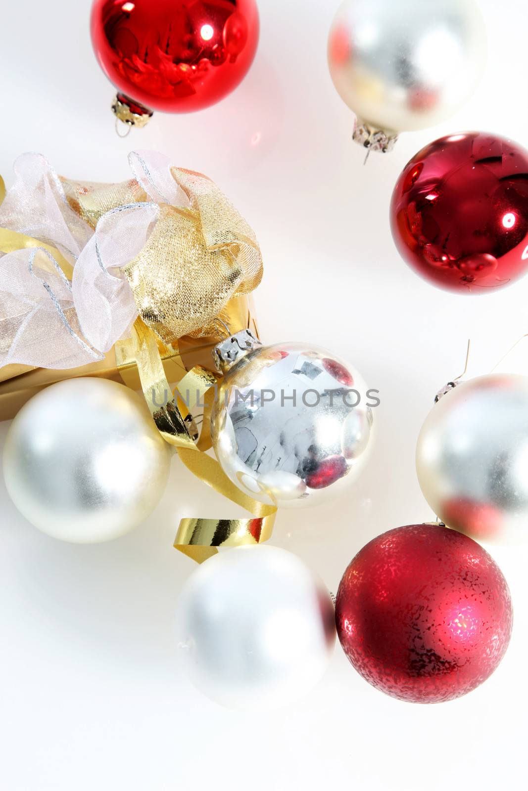 Overhead view on white of scattered red and white Christmas baubles with a decorative gold ribbon