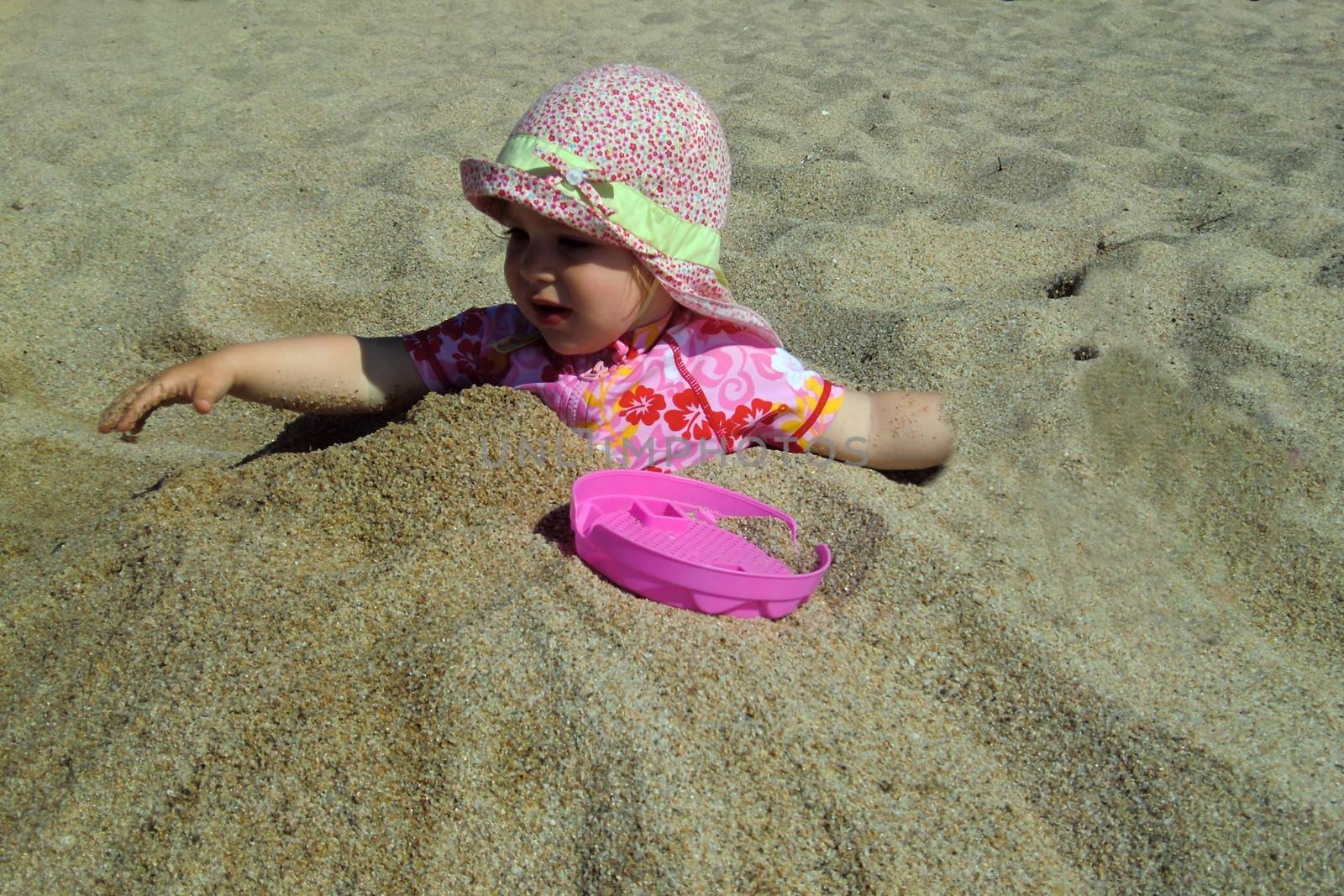 Portrait of little cute blond girl (one year and seven months of age) buried in the sand