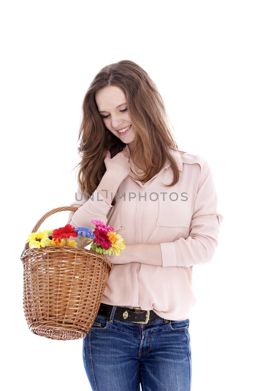 Smiling young teenage girl with a wicker basket of fresh flowers on her arm looking down at them with a smile, isolated on white