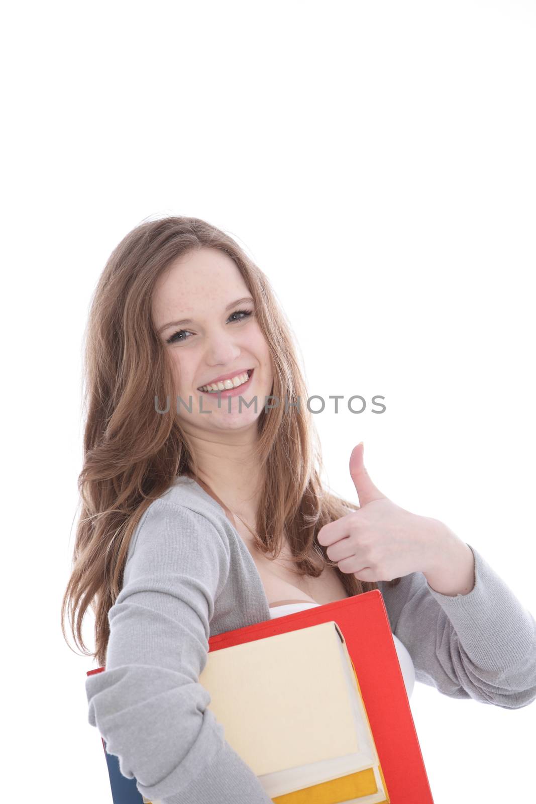 Happy vivacious young woman carrying her college textbooks under her arm giving a thumbs up gesture of approval and success isolated on white