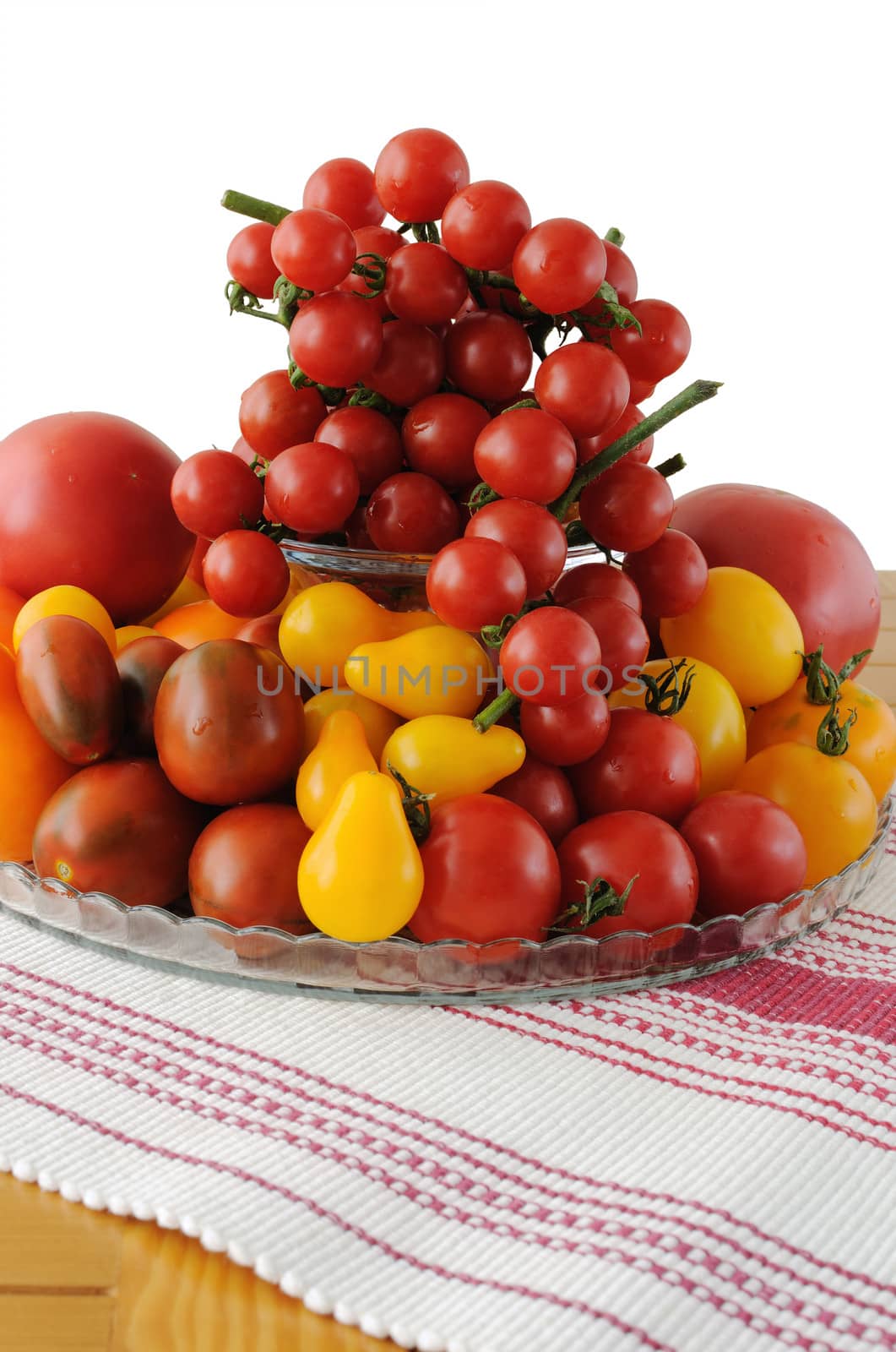 Different varieties of tomatoes in a glass vase on a napkin