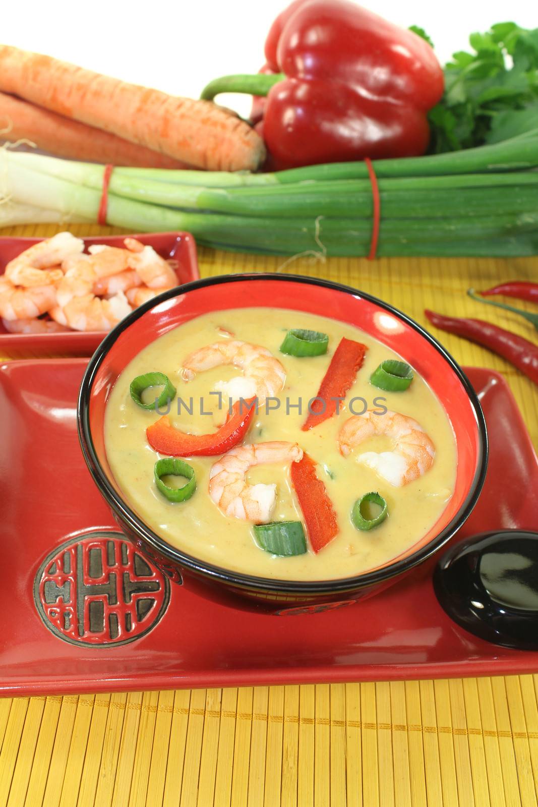 Curry soup with shrimp, red pepper, leeks and coconut milk on bright background