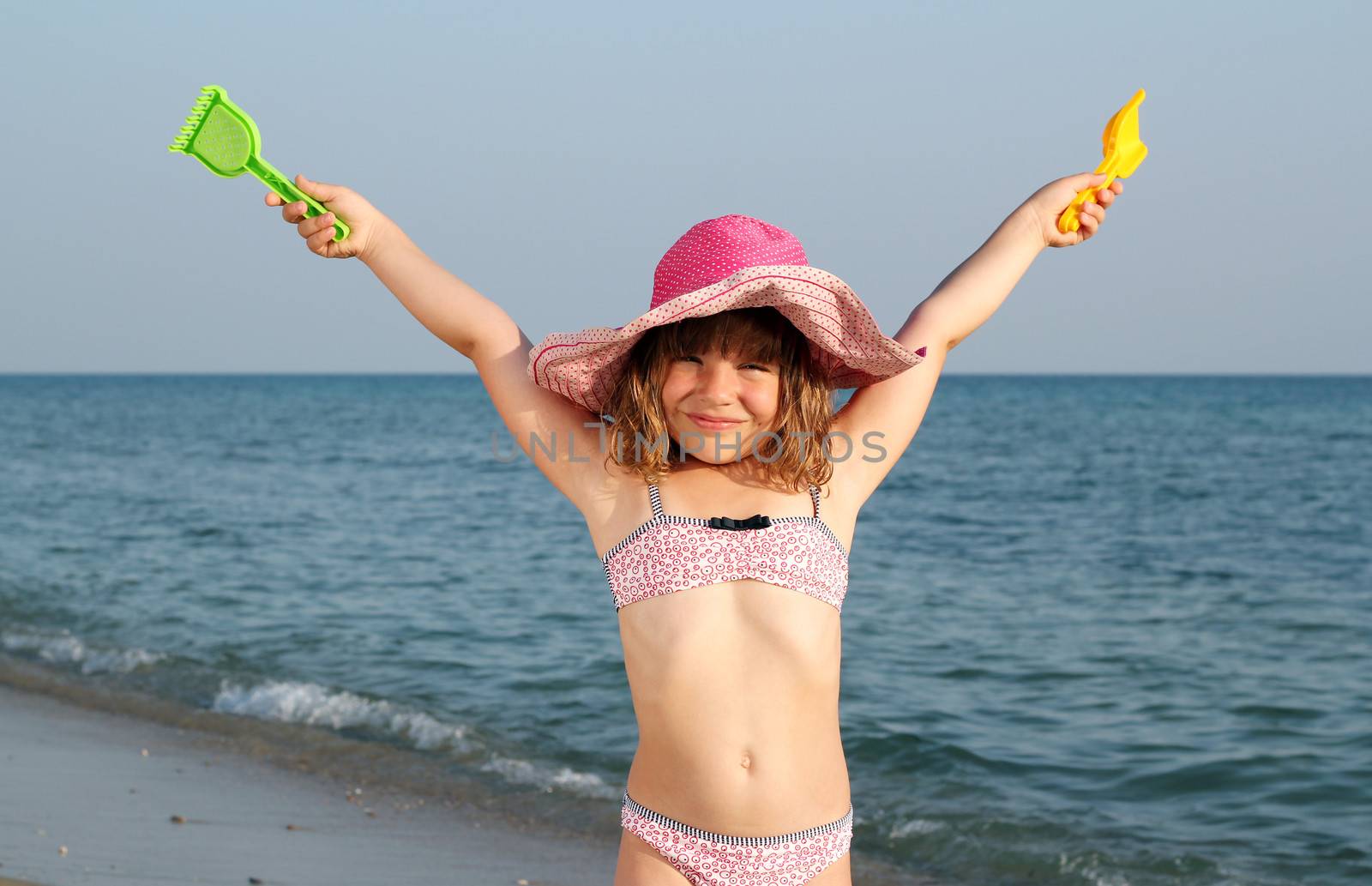happy little girl with hands up on beach