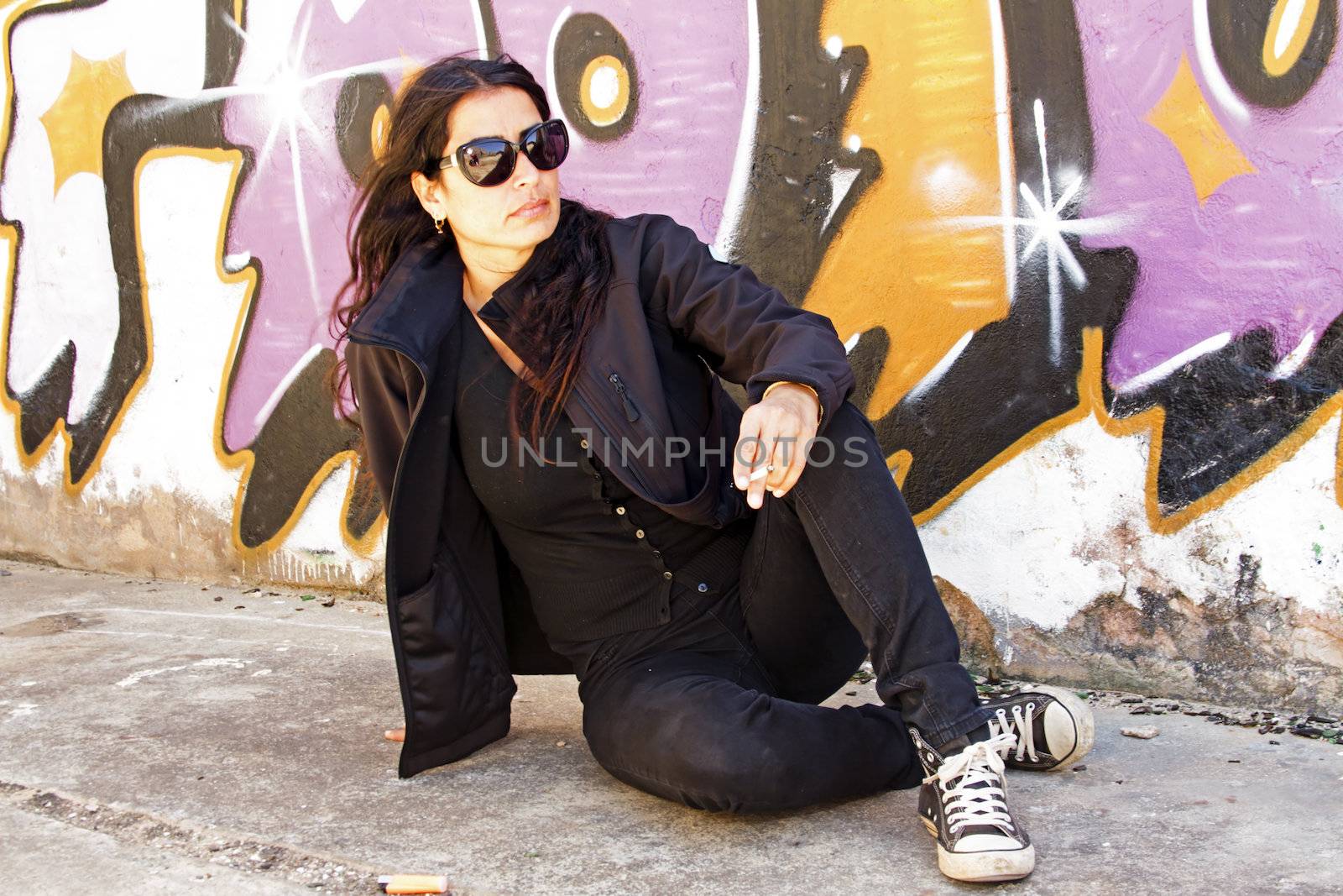 Smoking woman in black at the graffiti brick wall